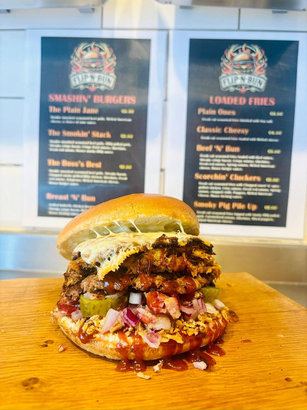 A stacked Flip n Bun smash burger in front of the van menu boards